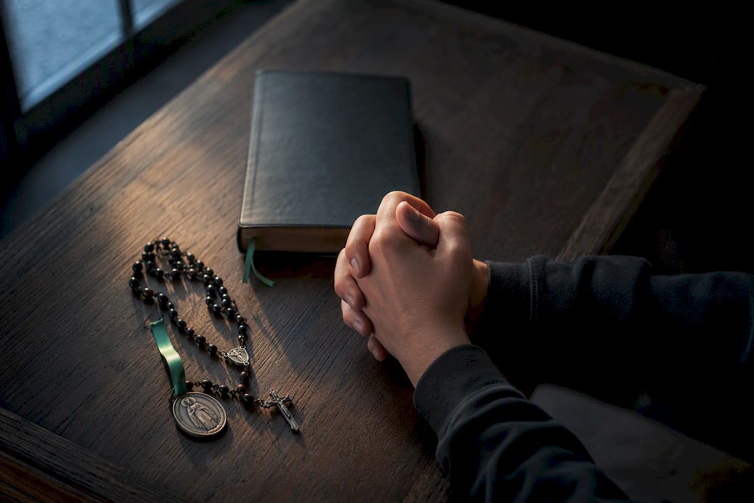 Hands praying beside rosary and angel medal